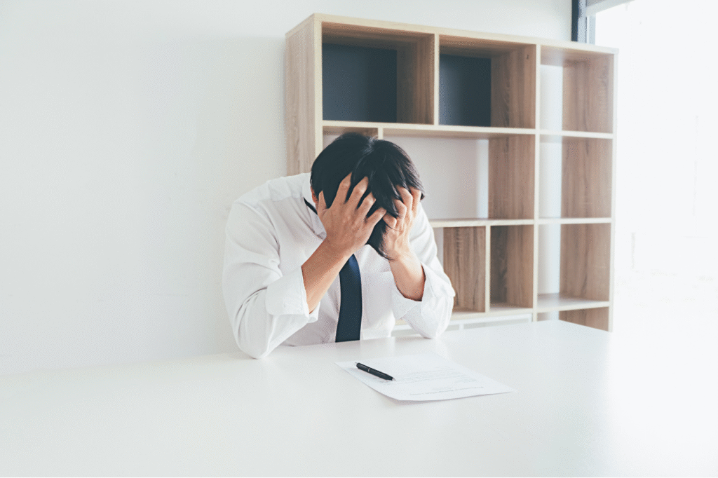 Frustrated businessman holding his head over paperwork, illustrating the stress of a rejected Japan Startup Visa application.